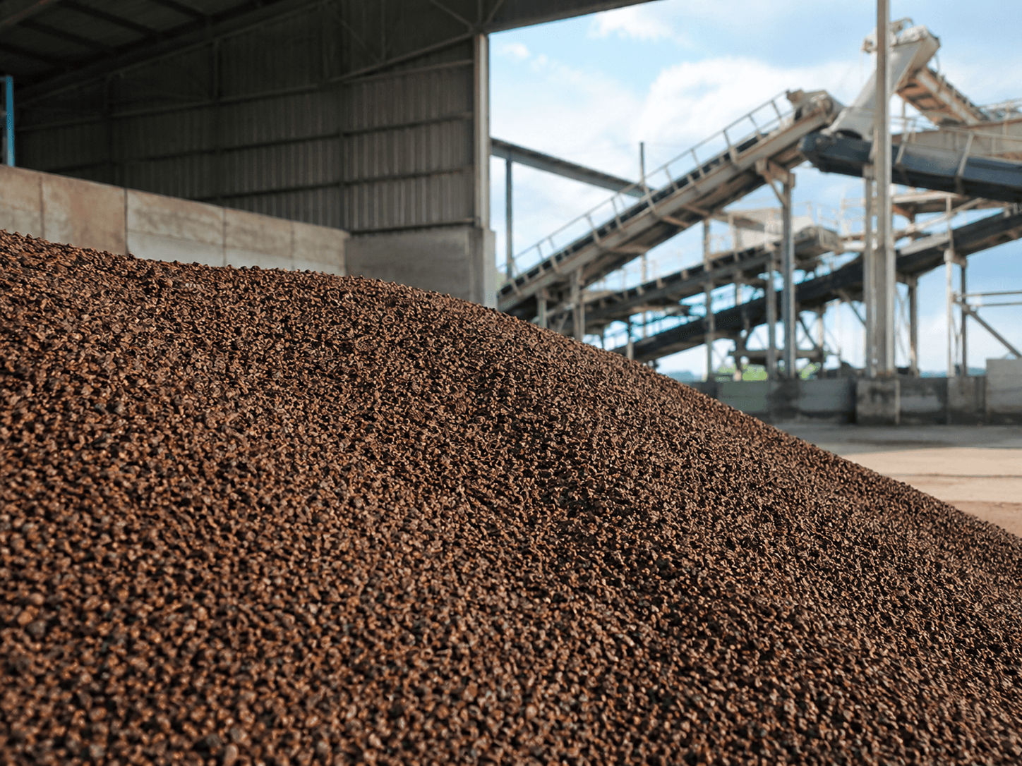 A heap of bulk granulated biomass beside a conveyor under an open shed