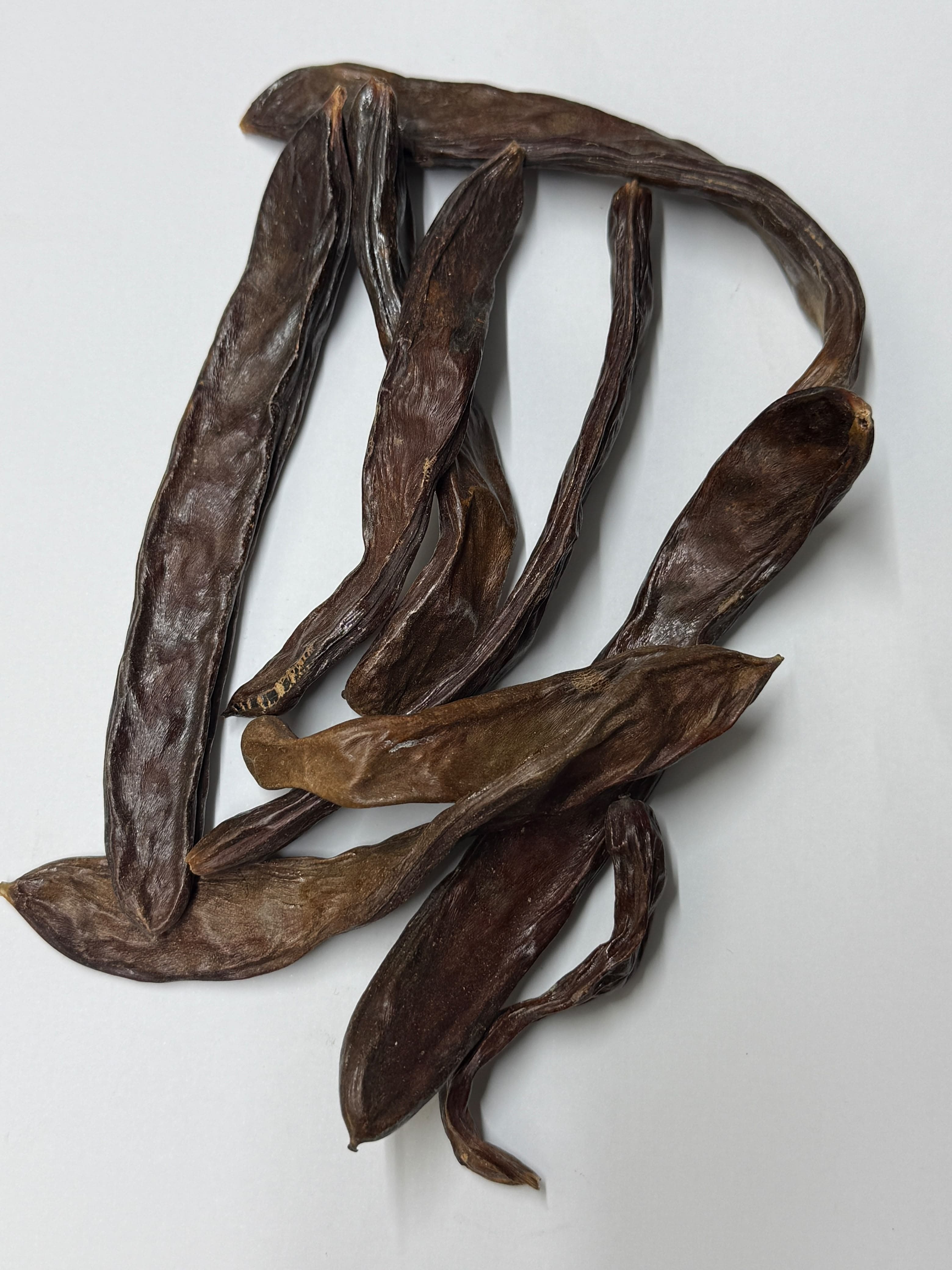 Several dried carob pods, photographed close up on a neutral background